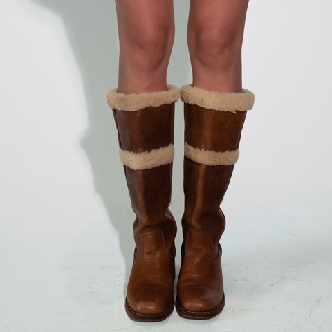 Brown leather boots with fur trim worn by a person on a white background
