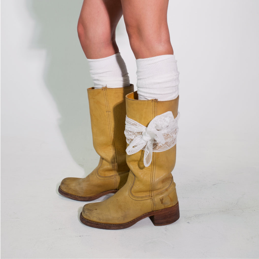 Brown knee-high boots with lace details worn with white socks on a light gray background