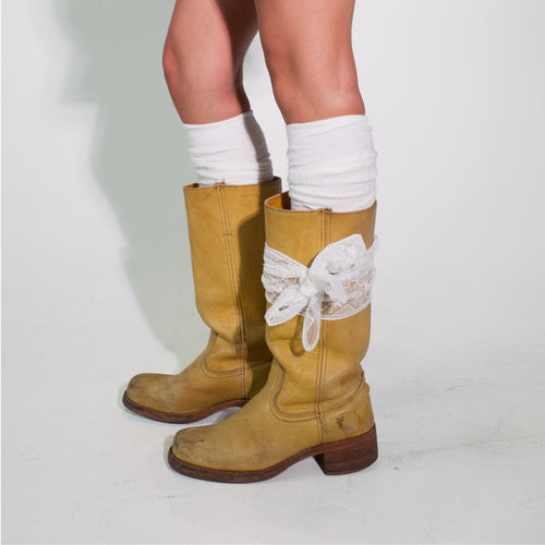 Brown knee-high boots with lace details worn with white socks on a light gray background