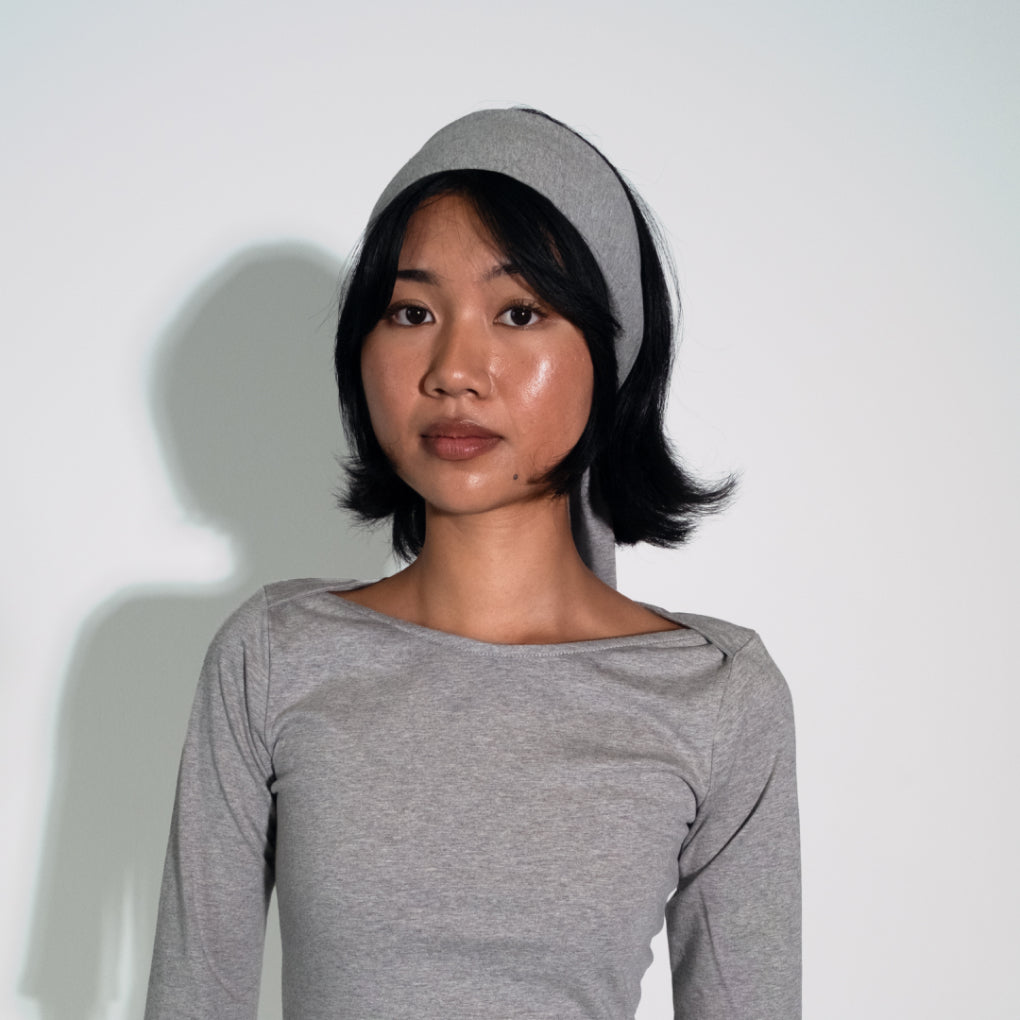 Woman wearing a gray long-sleeve top and headband against a white background