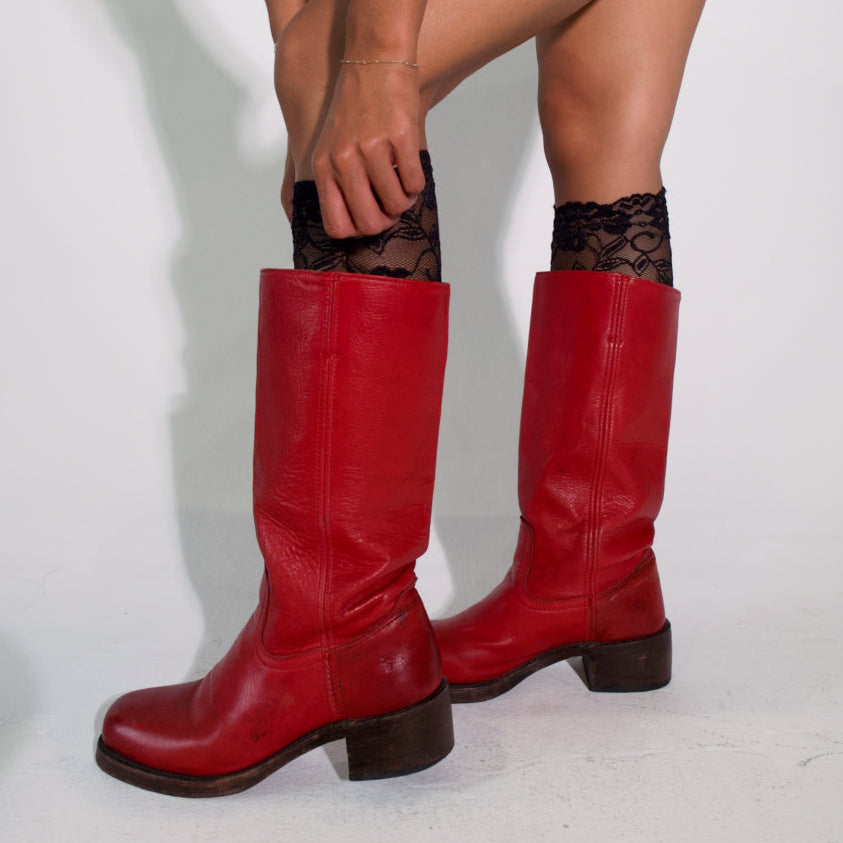 Red knee-high boots being worn with black tights on a light gray background