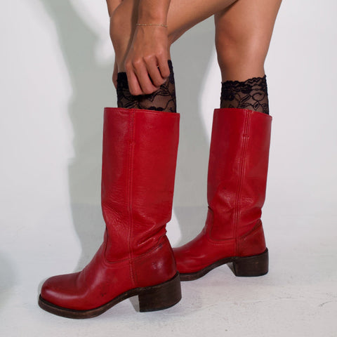 Red knee-high boots being worn with black tights on a light gray background