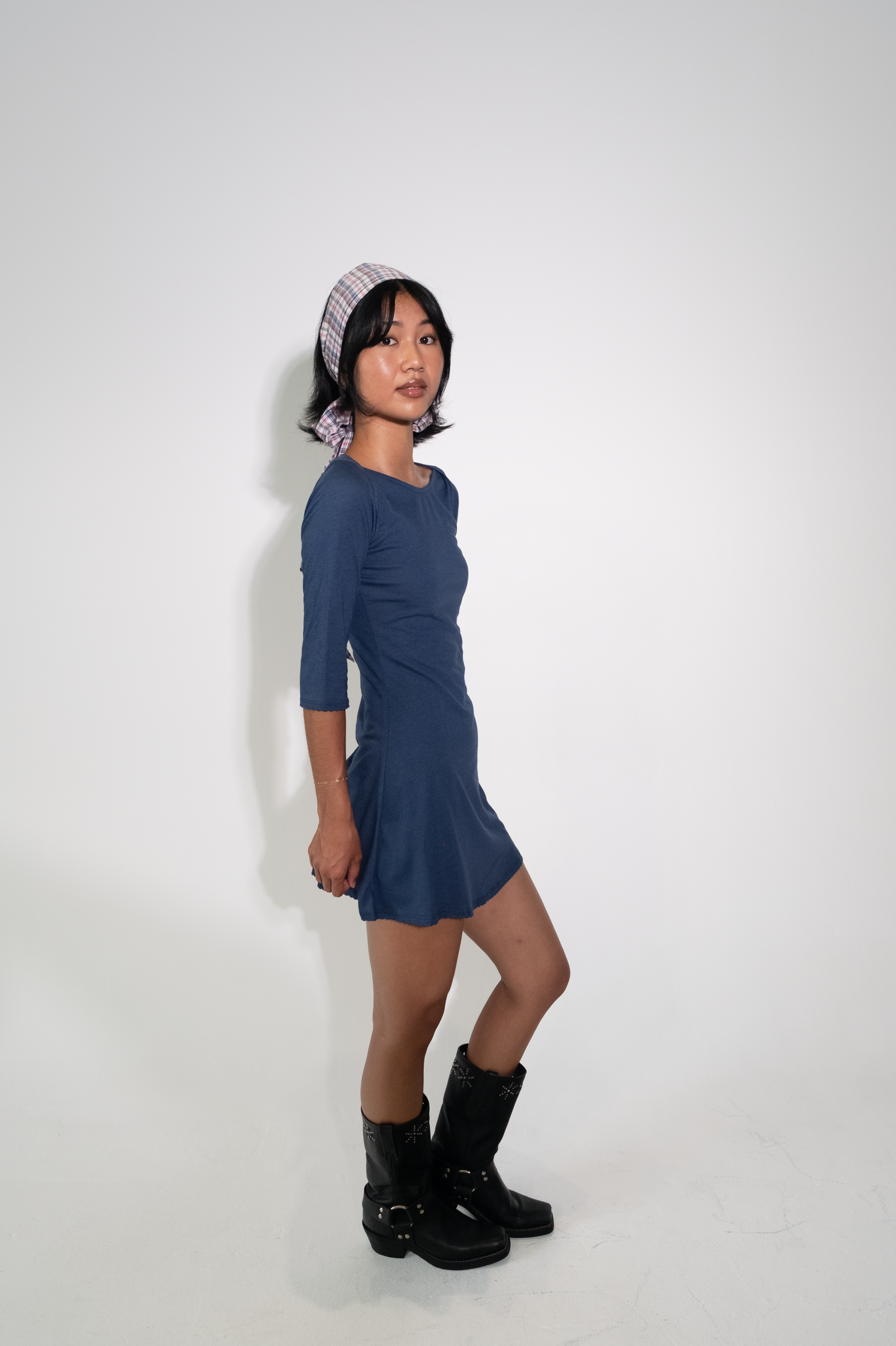 Woman wearing a blue dress and black boots against a white background