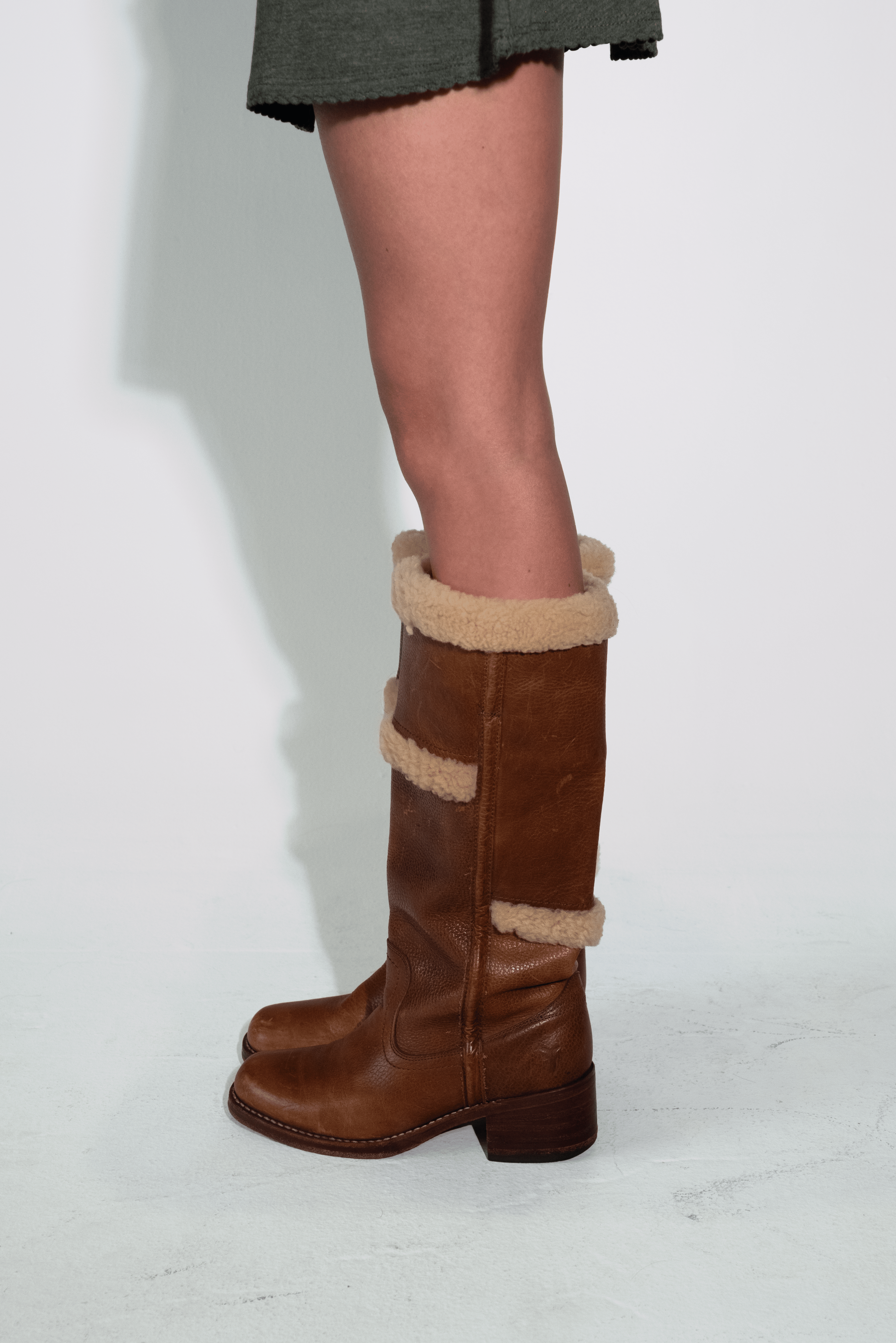 Brown knee-high boots with beige fur trim worn by a person on a white background