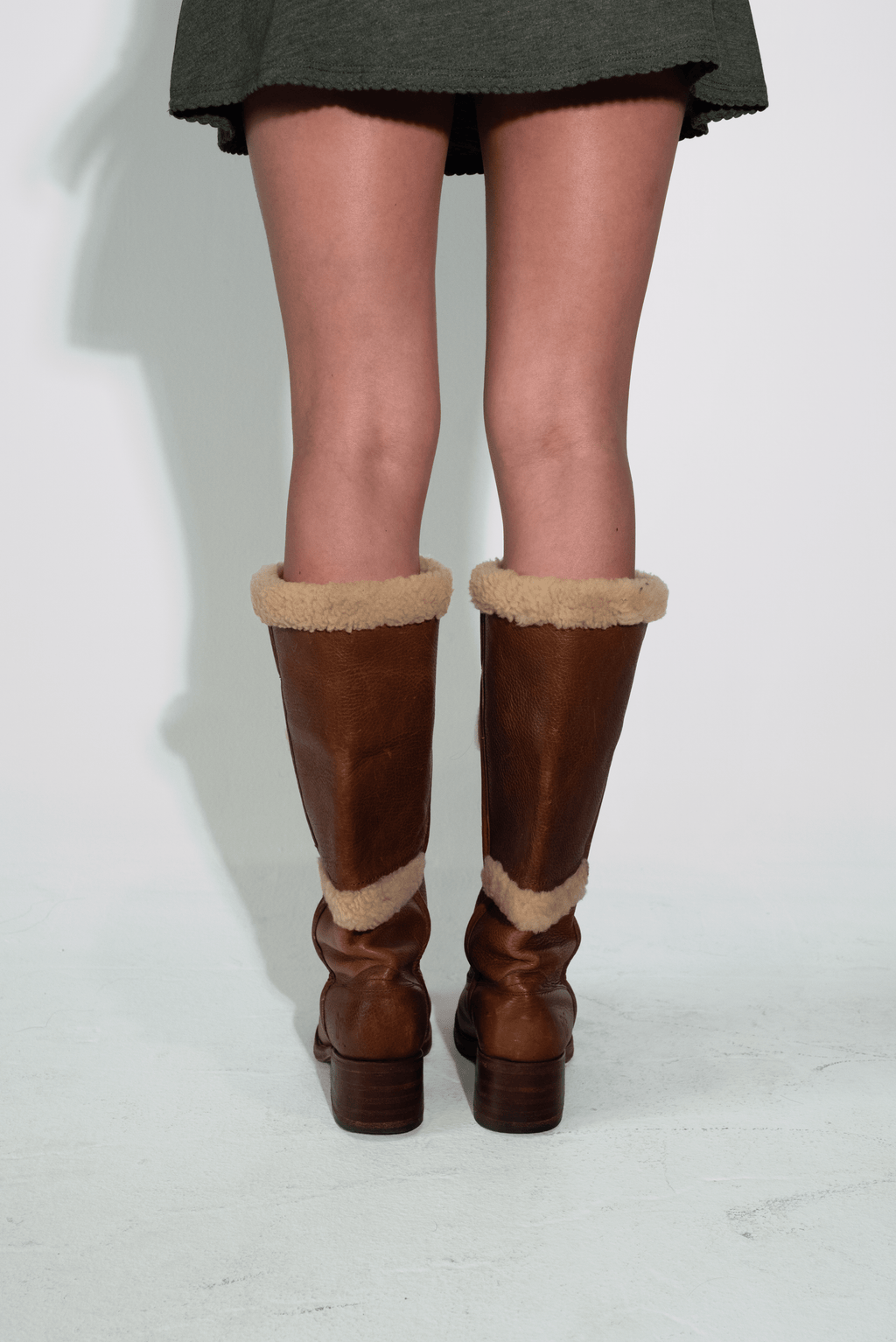 Brown knee-high boots with fur trim worn by a person on a white background