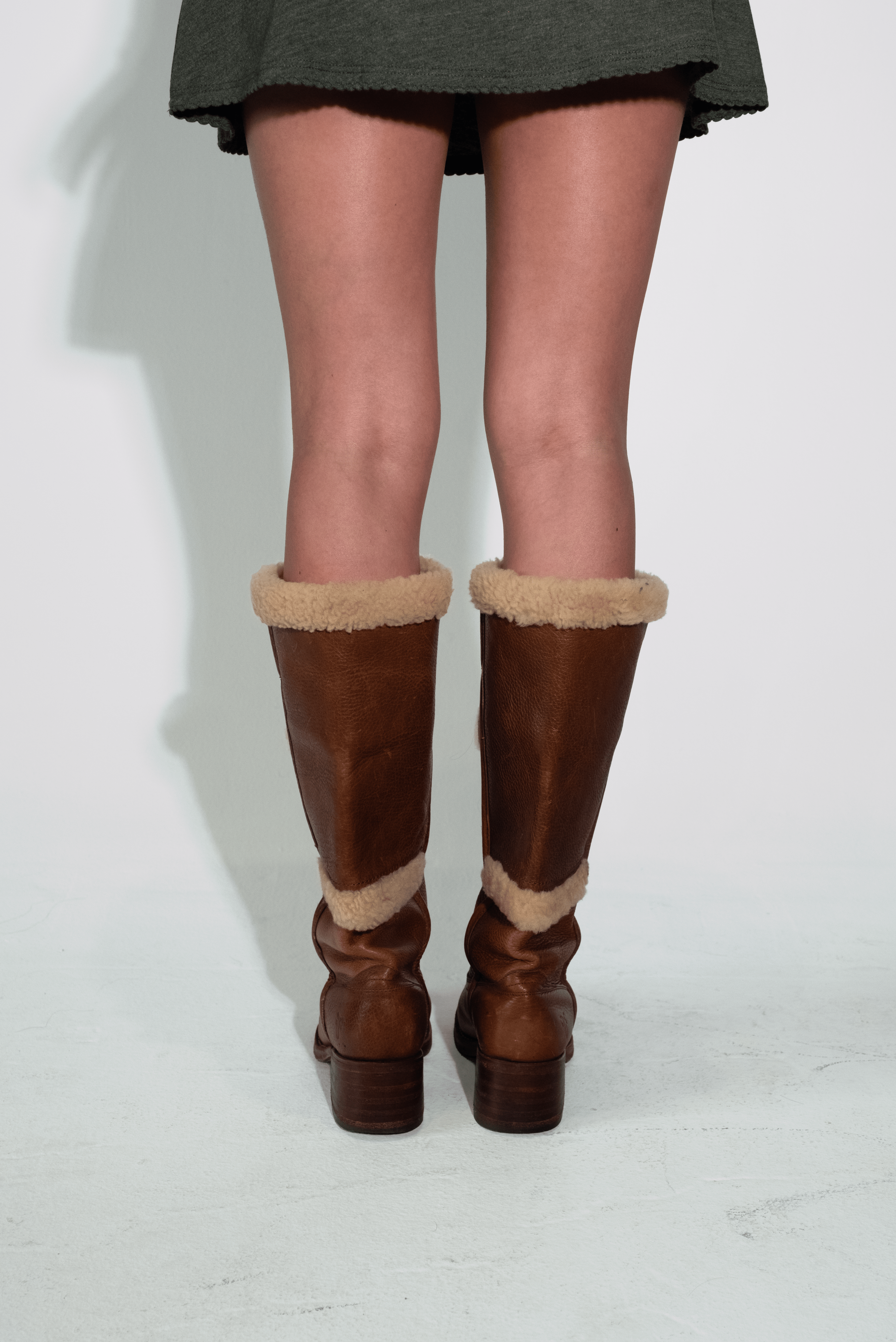 Brown knee-high boots with fur trim worn by a person on a white background