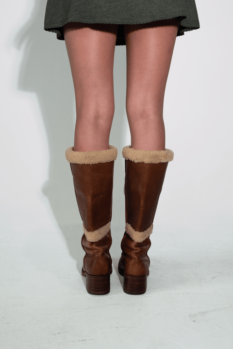 Brown knee-high boots with fur trim worn by a person on a white background