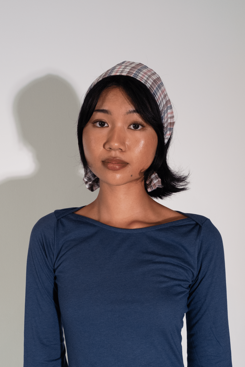 Woman wearing a blue dress with a plaid headband against a white background