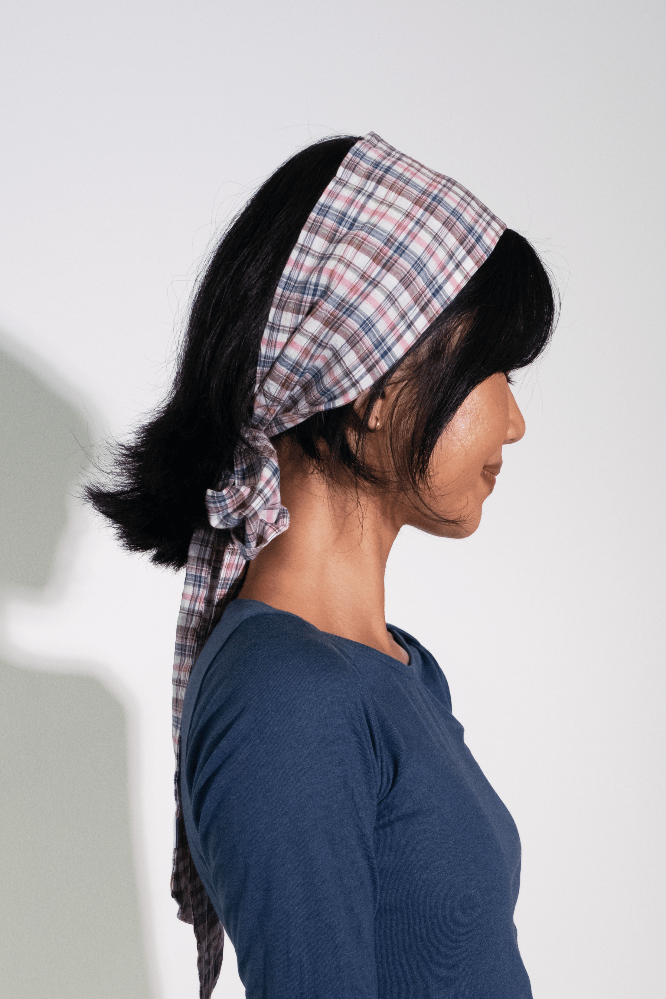 Woman wearing a blue dress and plaid headscarf against a white background