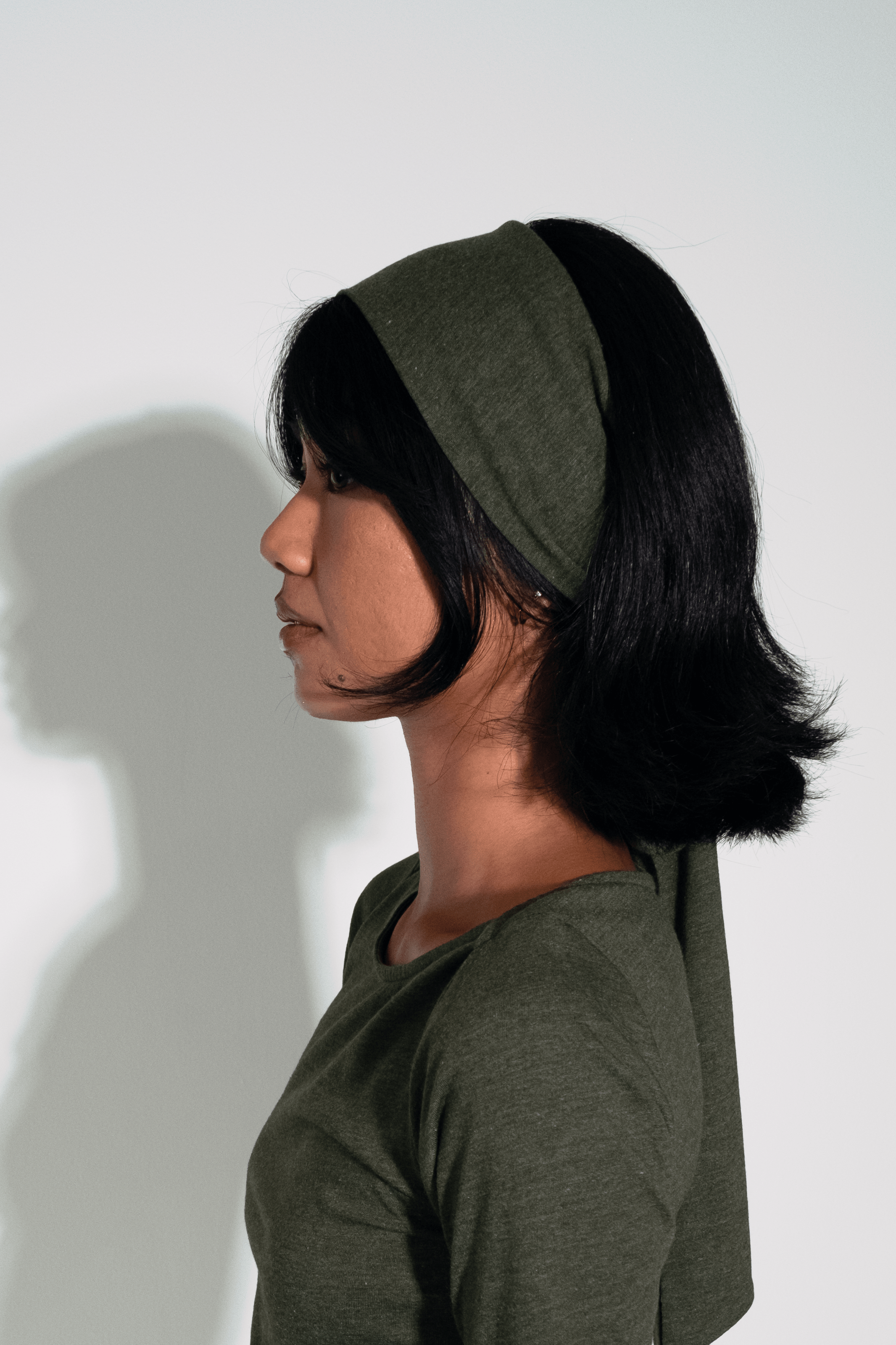 Woman wearing an olive green dress and headband against a white background