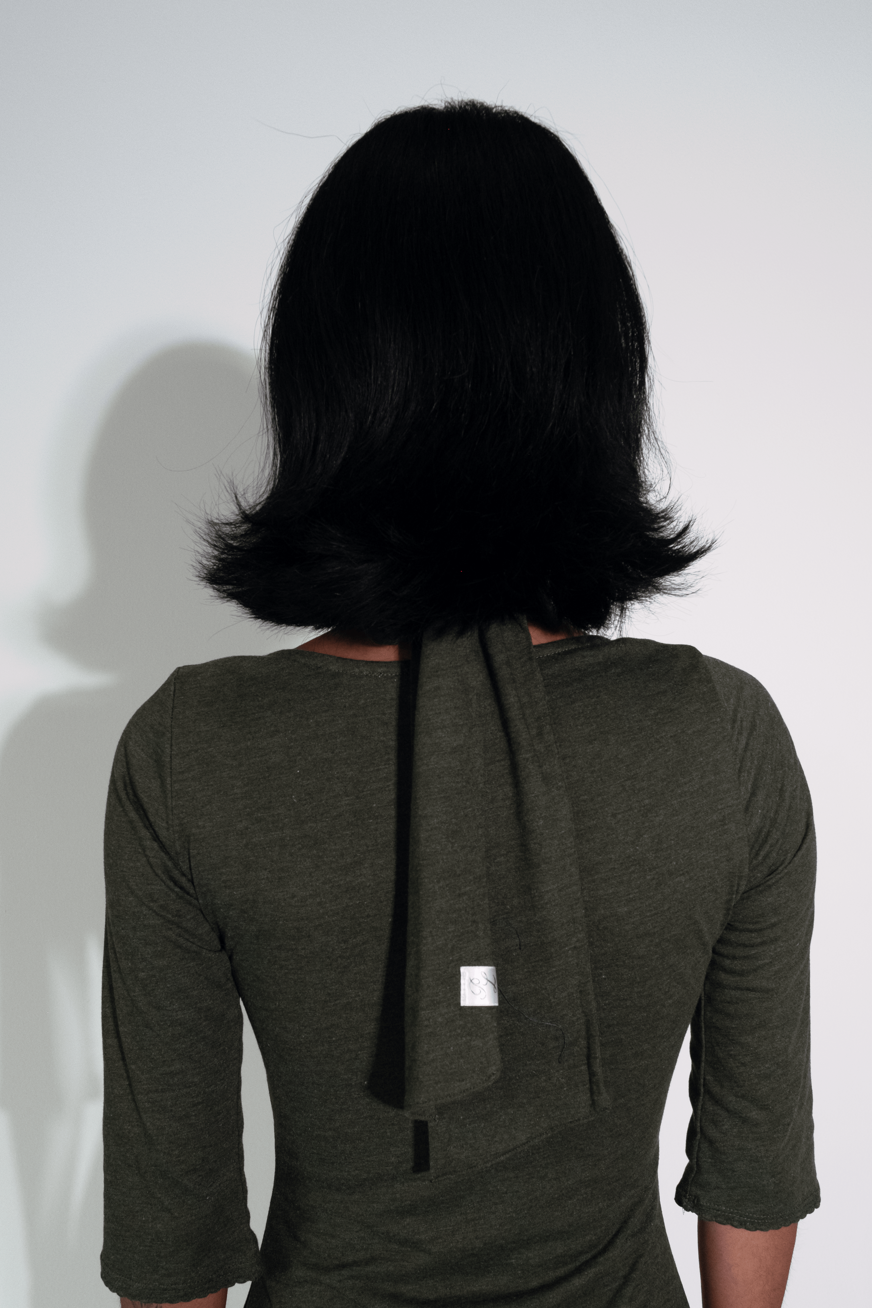 Person wearing a dark green dress with a black ribbon on a white background