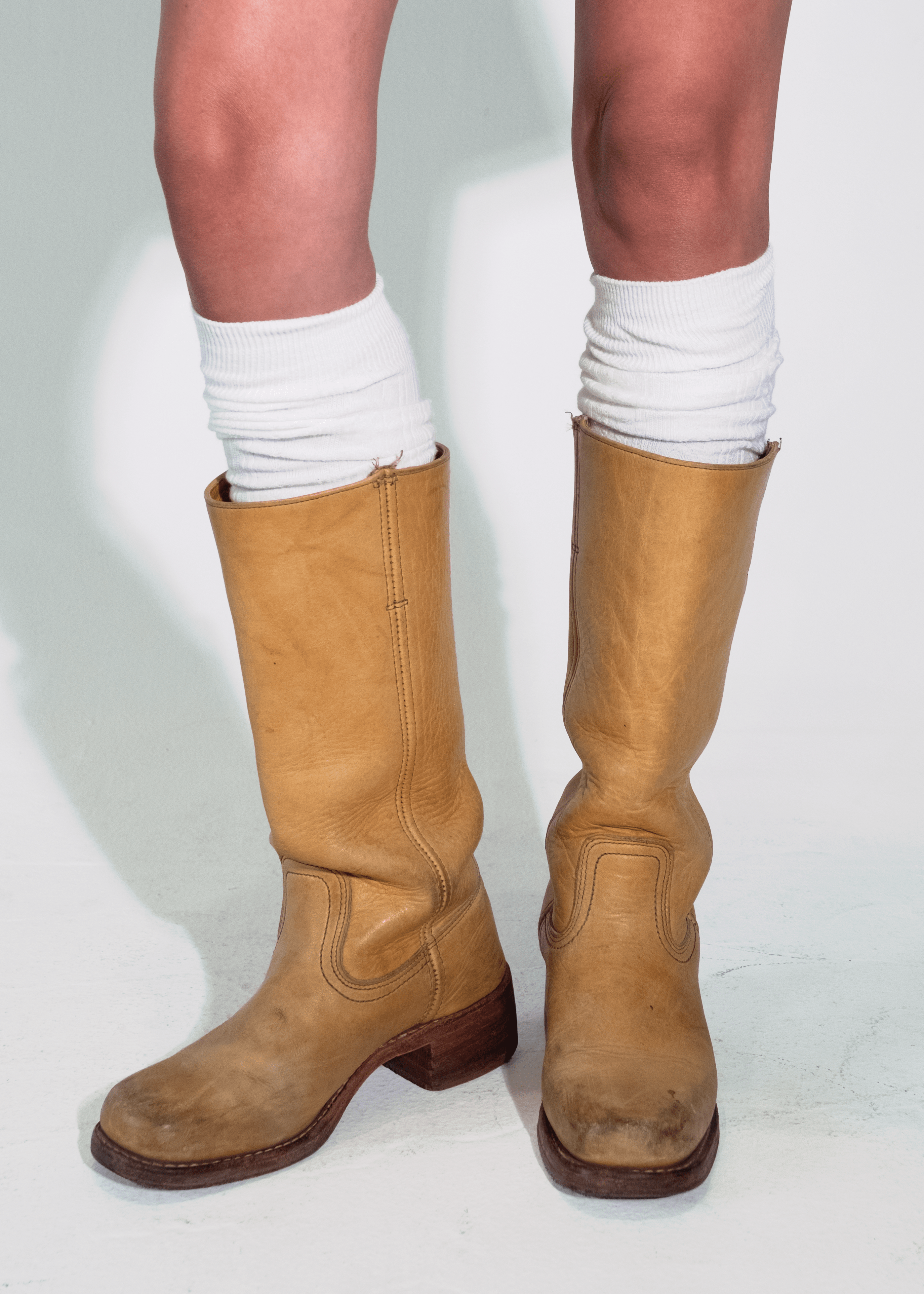 Person wearing tan knee-high boots with a plain background