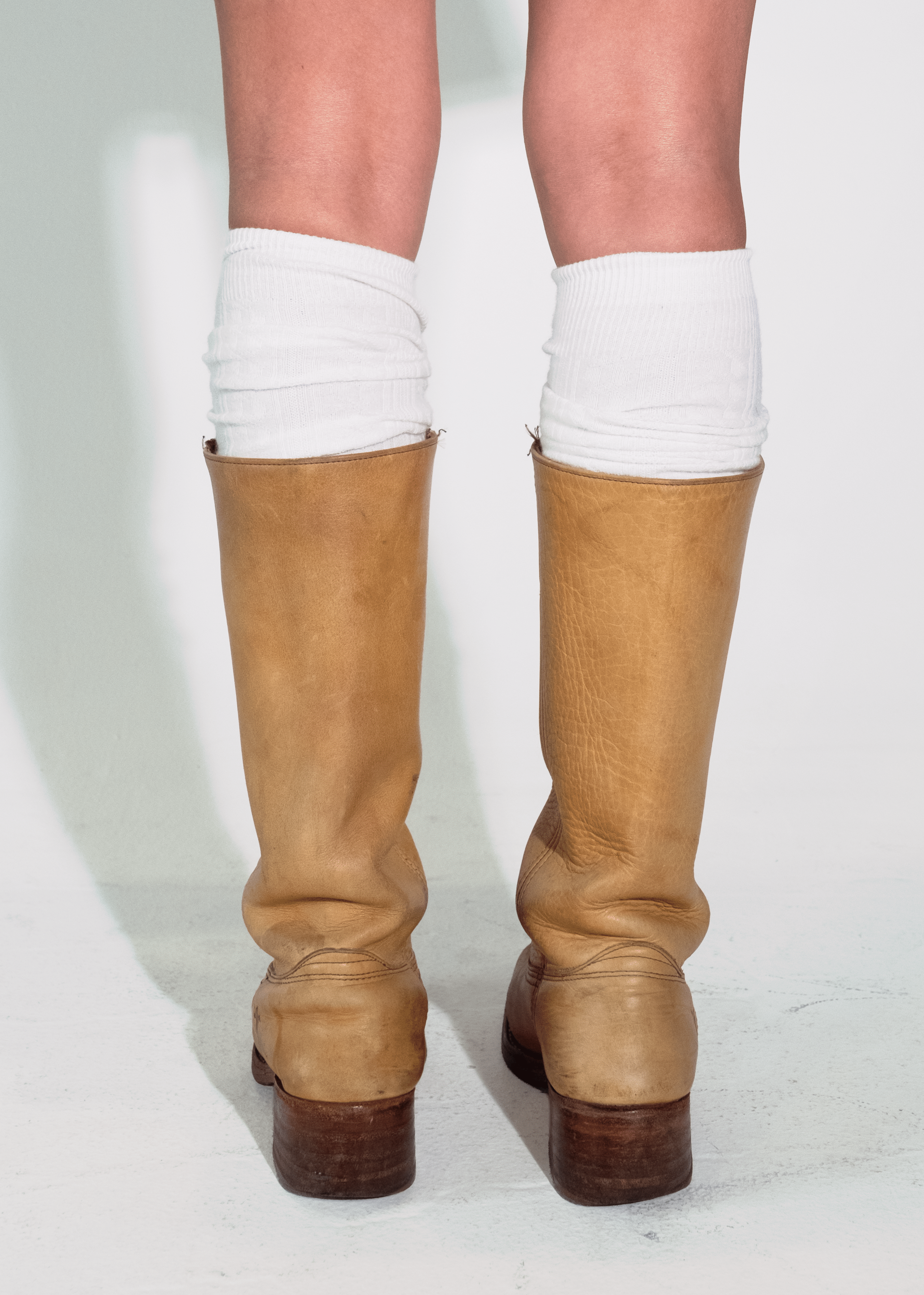 Tan knee-high boots with white socks on a plain background